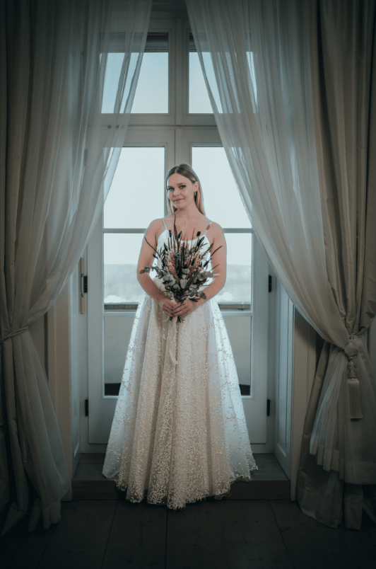Braut mit Brautstrauß vor Fenster